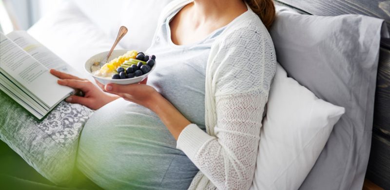 Femme enceinte qui mange des fruits en lisant un livre